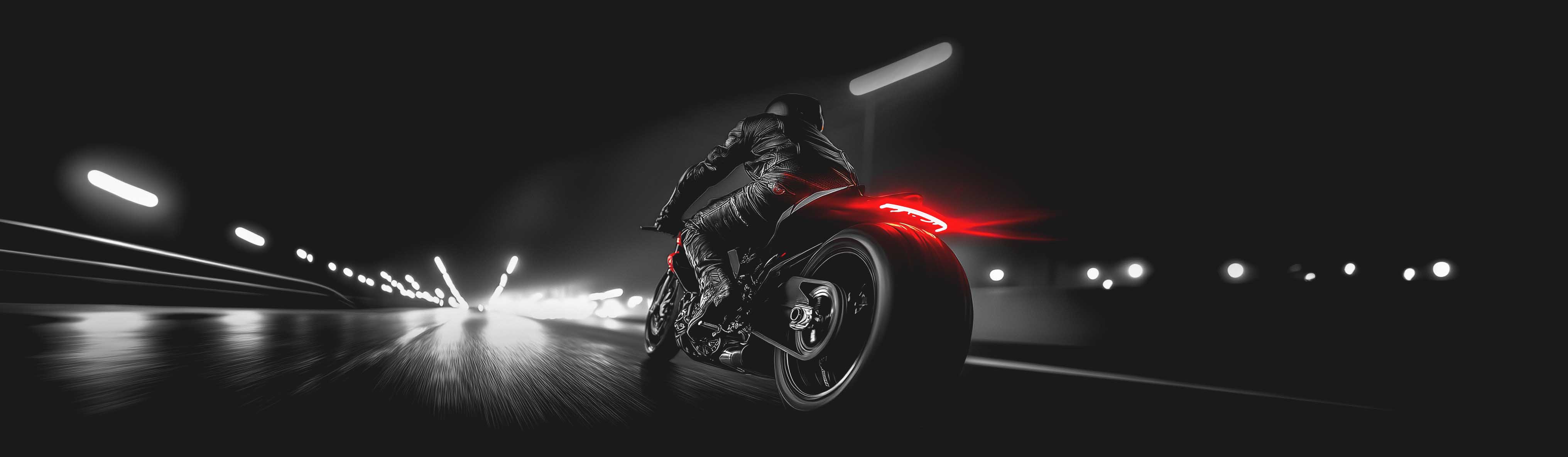 Panoramic photo of a lone motorbike racer seen from behind at night 